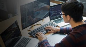 Digital marketing professional working on a laptop and desktop computer in a modern workspace.